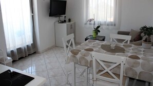 A dining area with a table set for four, a television on a stand, a small cabinet, and a potted plant. - Charming One-Bedroom Apartment for Two (Premantura)
