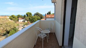 A balcony with two white metal chairs and a small table, overlooking a residential area with houses and trees. - Charming One-Bedroom Apartment for Two (Premantura)