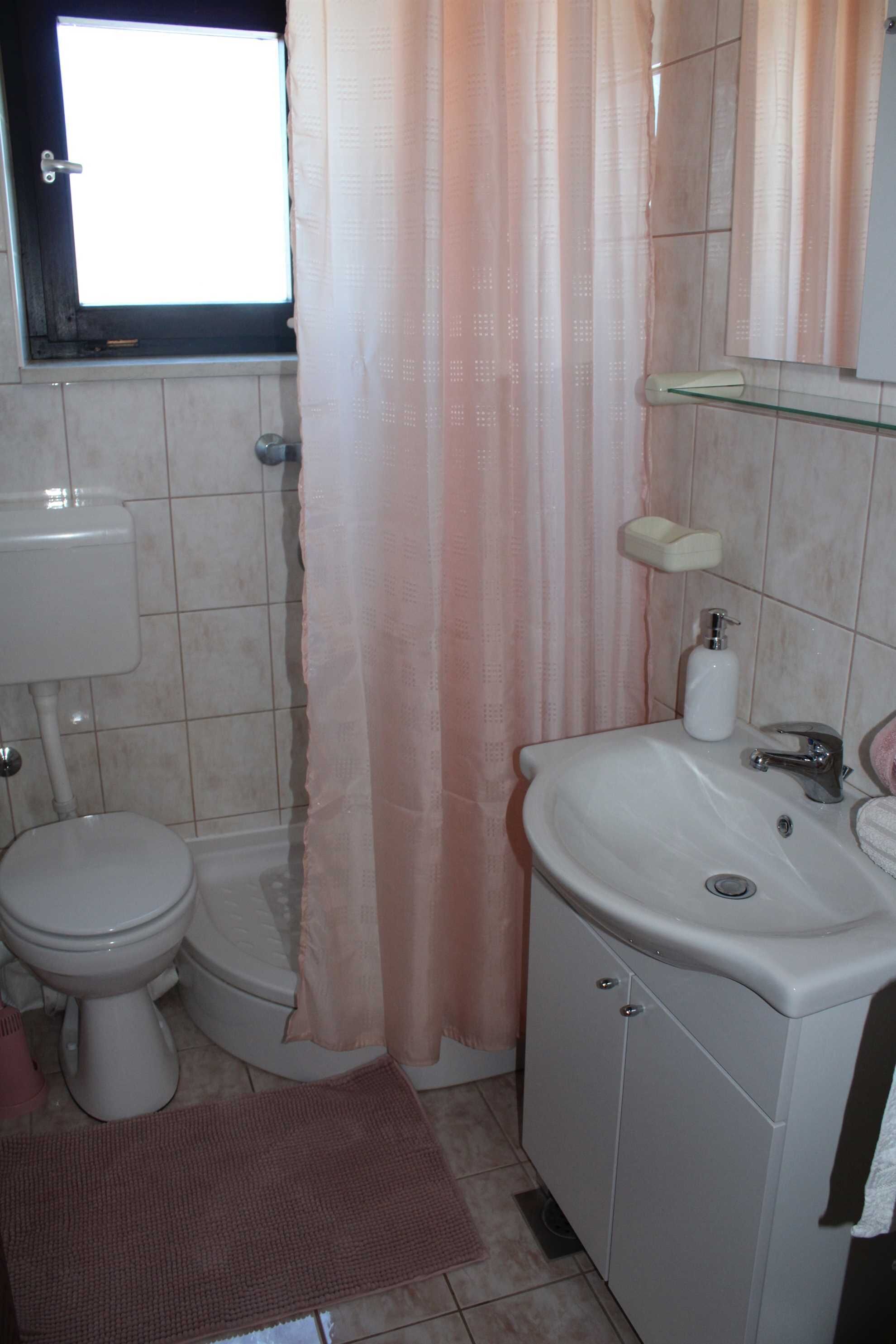 A bathroom with a toilet, sink, and a window with a curtain.