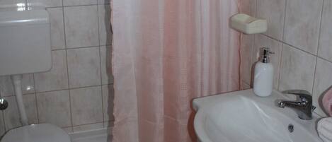 A bathroom with a toilet, sink, and a window with a curtain.