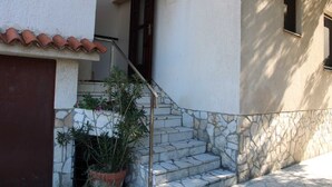 A stone staircase leading to a door with a metal railing, surrounded by potted plants and a tiled roof. - Charming One-Bedroom Apartment for Two (Premantura)