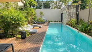 En swimmingpool med træterrasse, liggestole og plantekrukker.