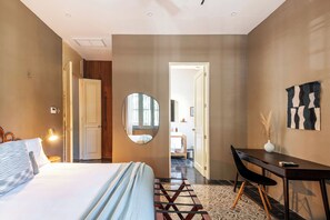 Une chambre d’hôtel moderne équipée d’un lit, d’un bureau et d’une chaise, d’un miroir et donnant sur la salle de bain.