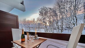 Un balcon avec une table en bois, une bouteille de champagne et des verres, donnant sur un paysage enneigé.