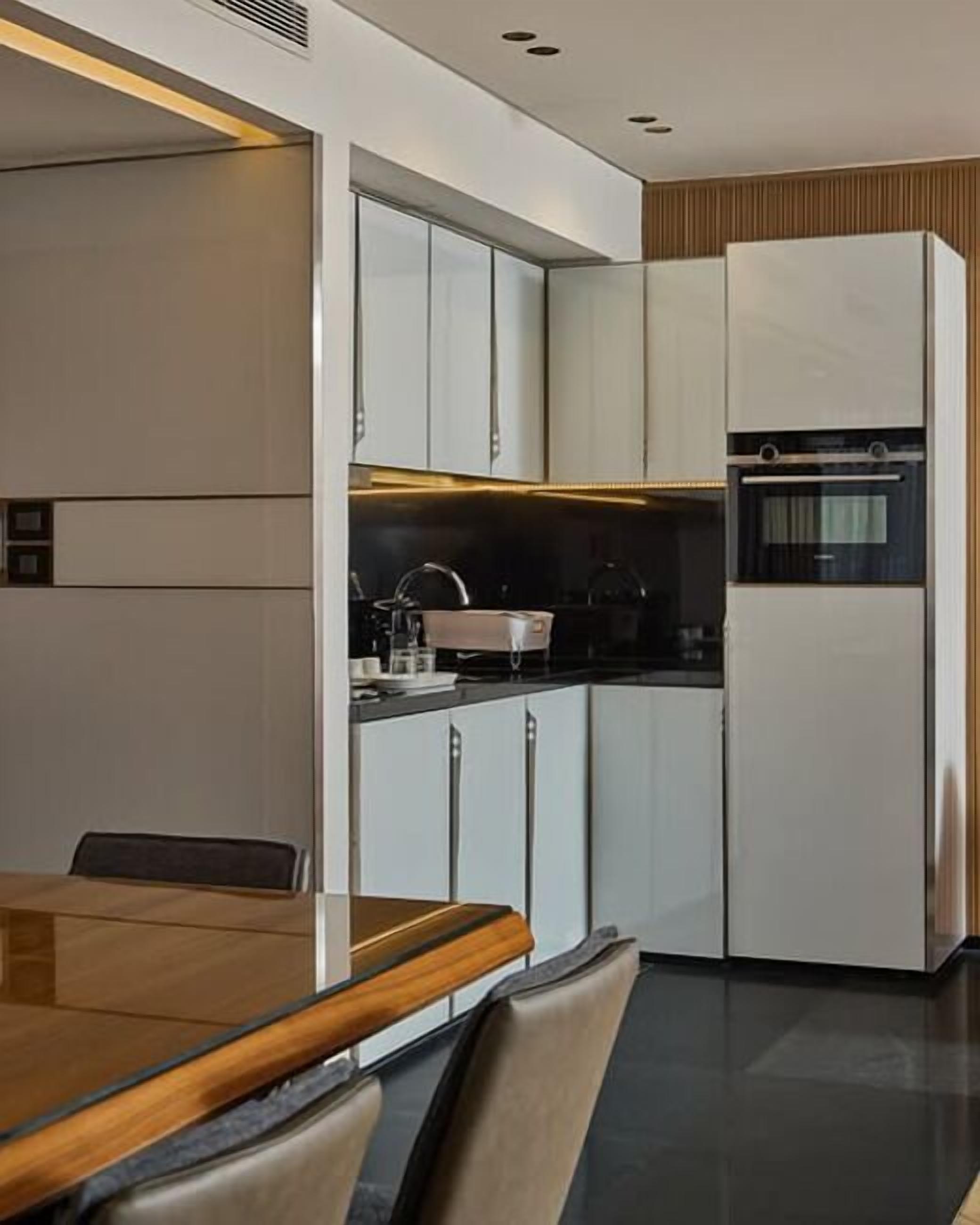 A modern kitchen with white cabinets, a built-in oven, and a dining area with a wooden table and chairs.