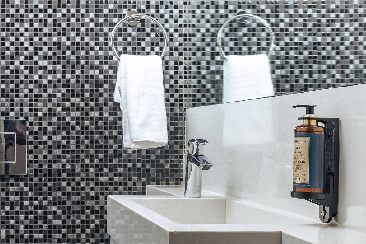 Un baño moderno con salpicadero de azulejos, un lavabo blanco, un inodoro y un cubo de basura.