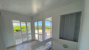 A spacious room with a large sliding glass door leading to a balcony with a view of greenery and a clear sky. - Cobertura Vista Mar Jurerê Internacional (Florianópolis)