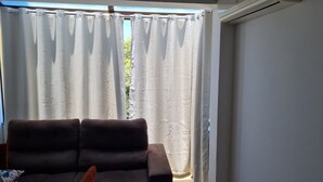 A room with a sofa and a window with white curtains. - Cobertura Vista Mar Jurerê Internacional (Florianópolis)