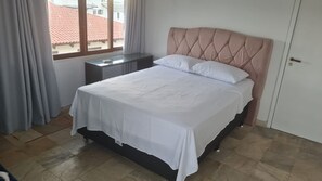 A bedroom with a bed, a nightstand, a window with curtains, and a door. - Cobertura Vista Mar Jurerê Internacional (Florianópolis)