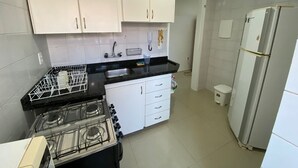 A kitchen with white cabinets, a black countertop, a gas stove, a sink, and a refrigerator. - Cobertura Vista Mar Jurerê Internacional (Florianópolis)