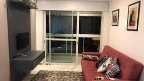 Una sala de estar con un sofá rojo, alfombra estampada y un televisor de pantalla plana sobre un soporte negro.
