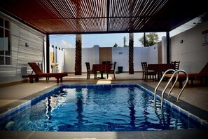 Una piscina interior con muelle de madera, sillas de descanso y una mesa con sillas.
