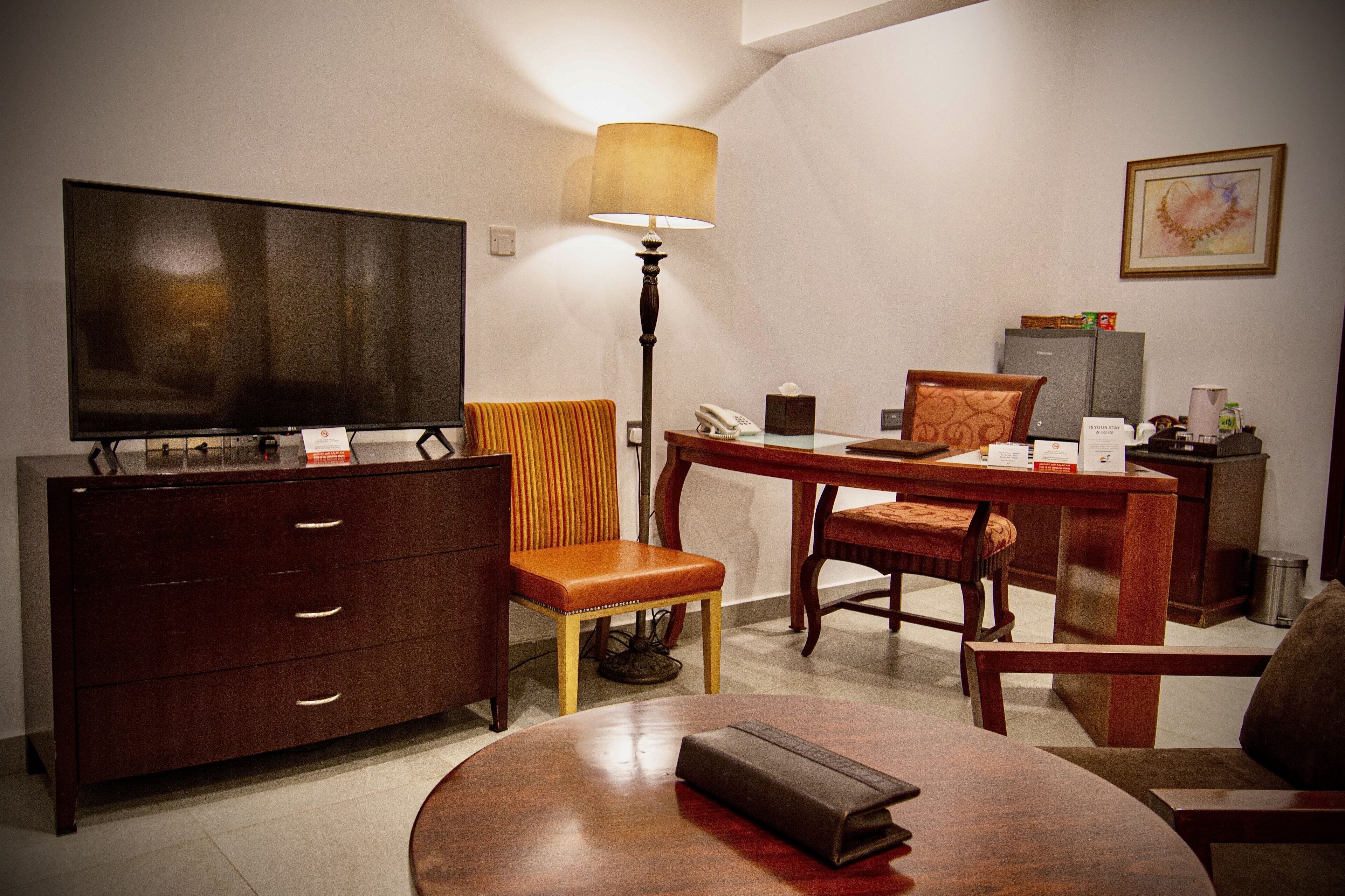 Une chambre d’hôtel équipée d’une télévision, d’un bureau avec une lampe, d’une chaise, d’un canapé et d’une petite table.