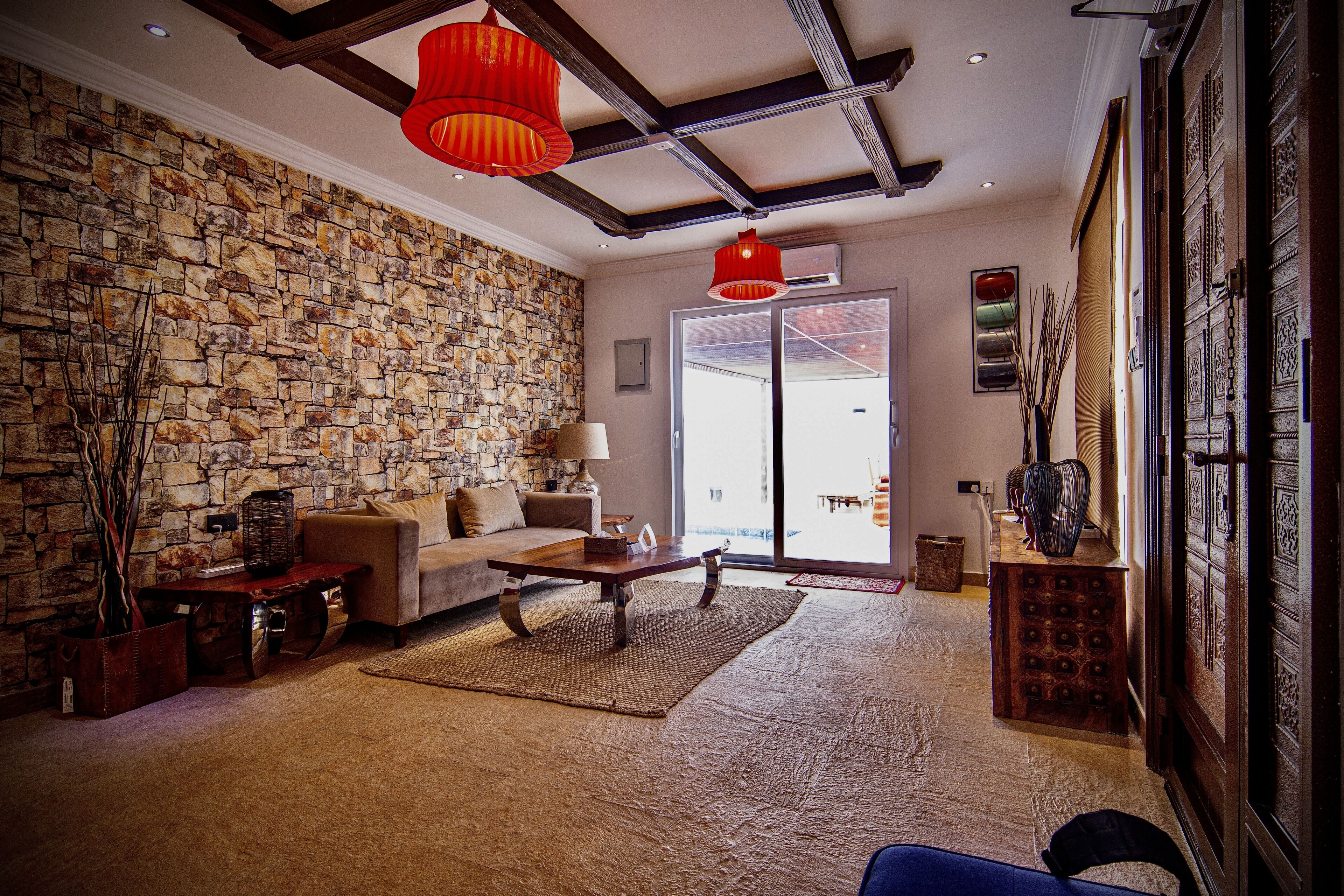 A cozy living room with a stone wall, a sofa, a coffee table, and a red pendant light.