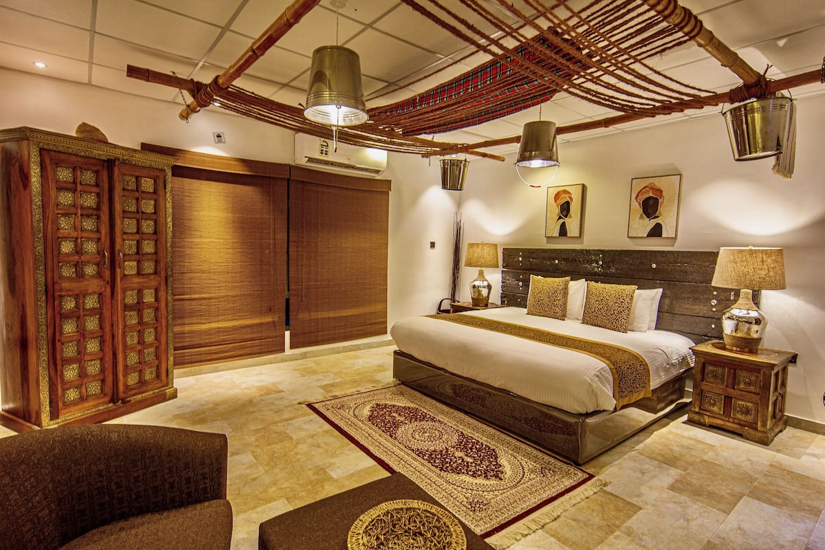 Um quarto espaçoso com uma cama grande, um guarda-roupa de madeira e um candeeiro pendente.