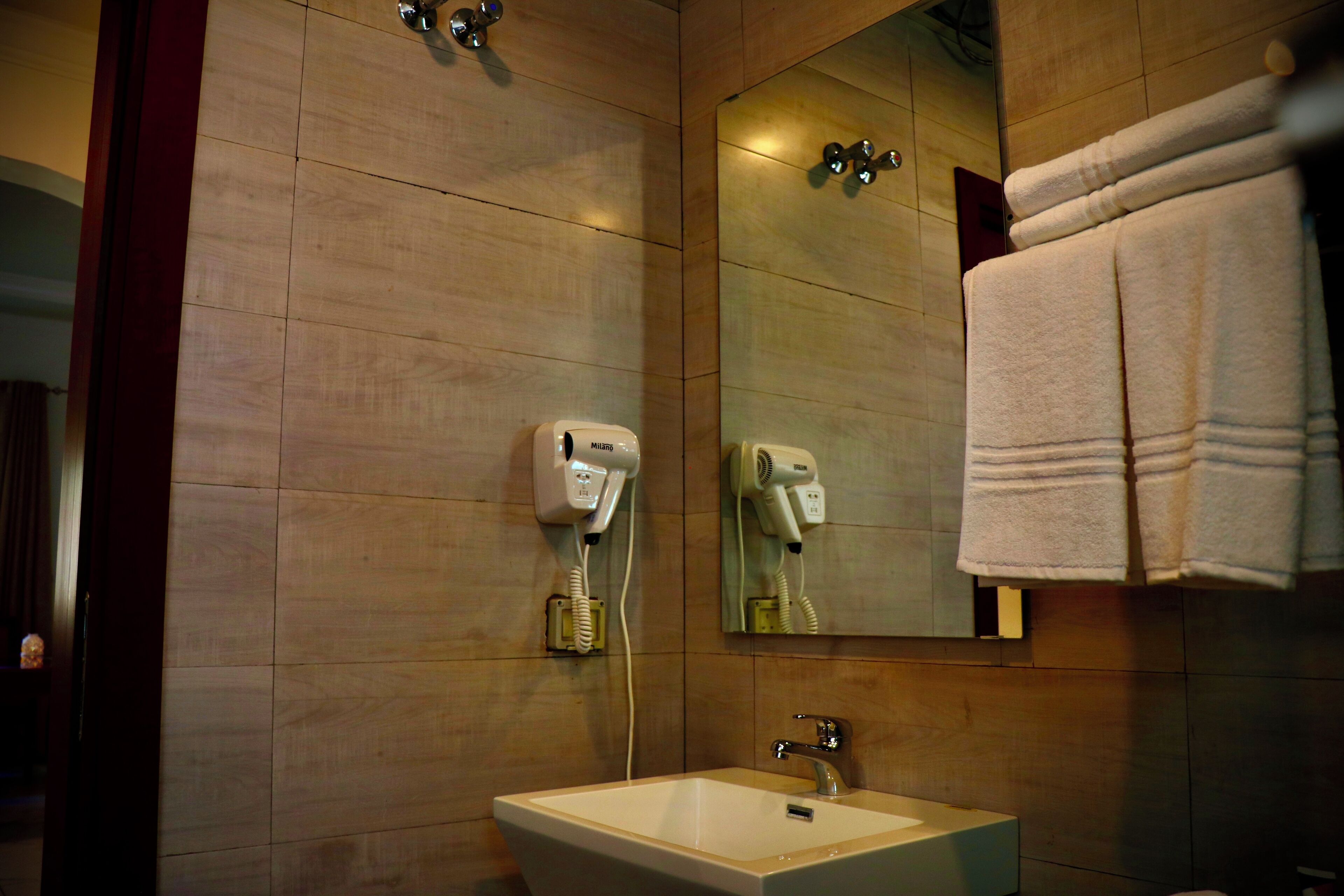 Une salle de bain équipée d’un lavabo, d’un miroir, d’un porte-serviettes et de deux sèche-cheveux fixés au mur.