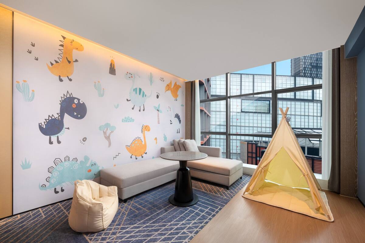 Ein modernes Zimmer mit einer Couch, einem kleinen runden Tisch, einem Zelt und einer Wand mit verspielten Dinosaurier- und Tierstickern.
