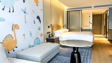 Una habitación de hotel con una cama, una mesita de noche, una lámpara, un sofá y un papel pintado con motivos de dinosaurios.