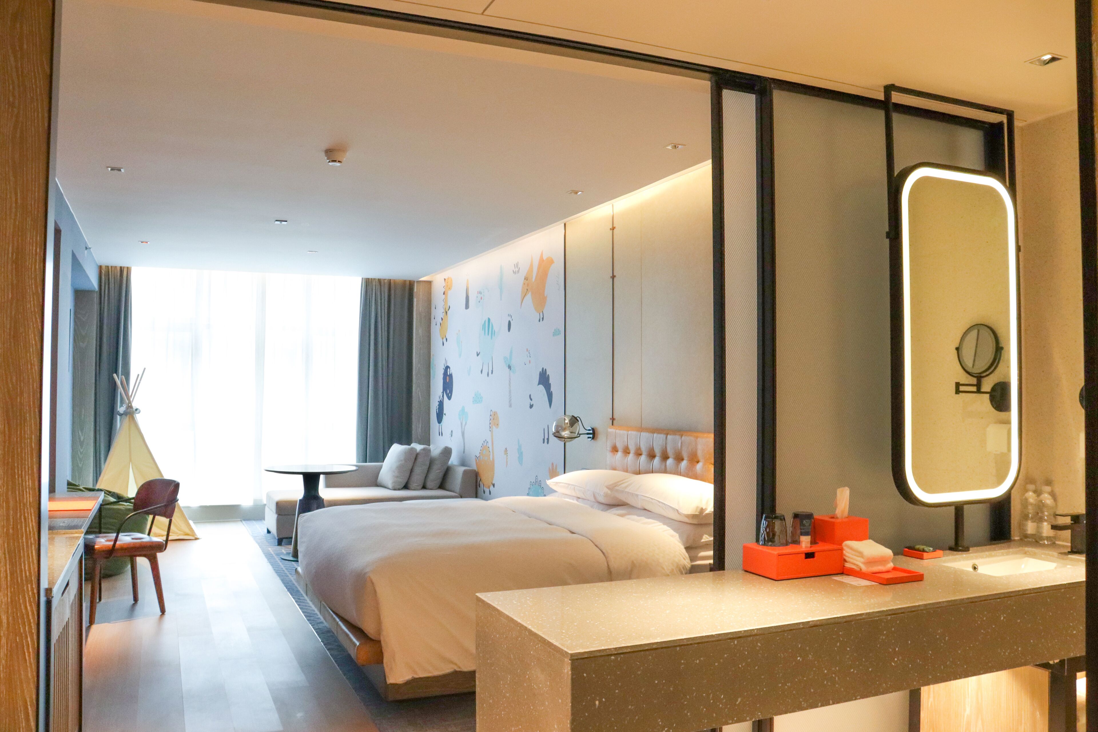 Habitación de hotel con cama, mesita de noche, espejo y vistas al exterior.