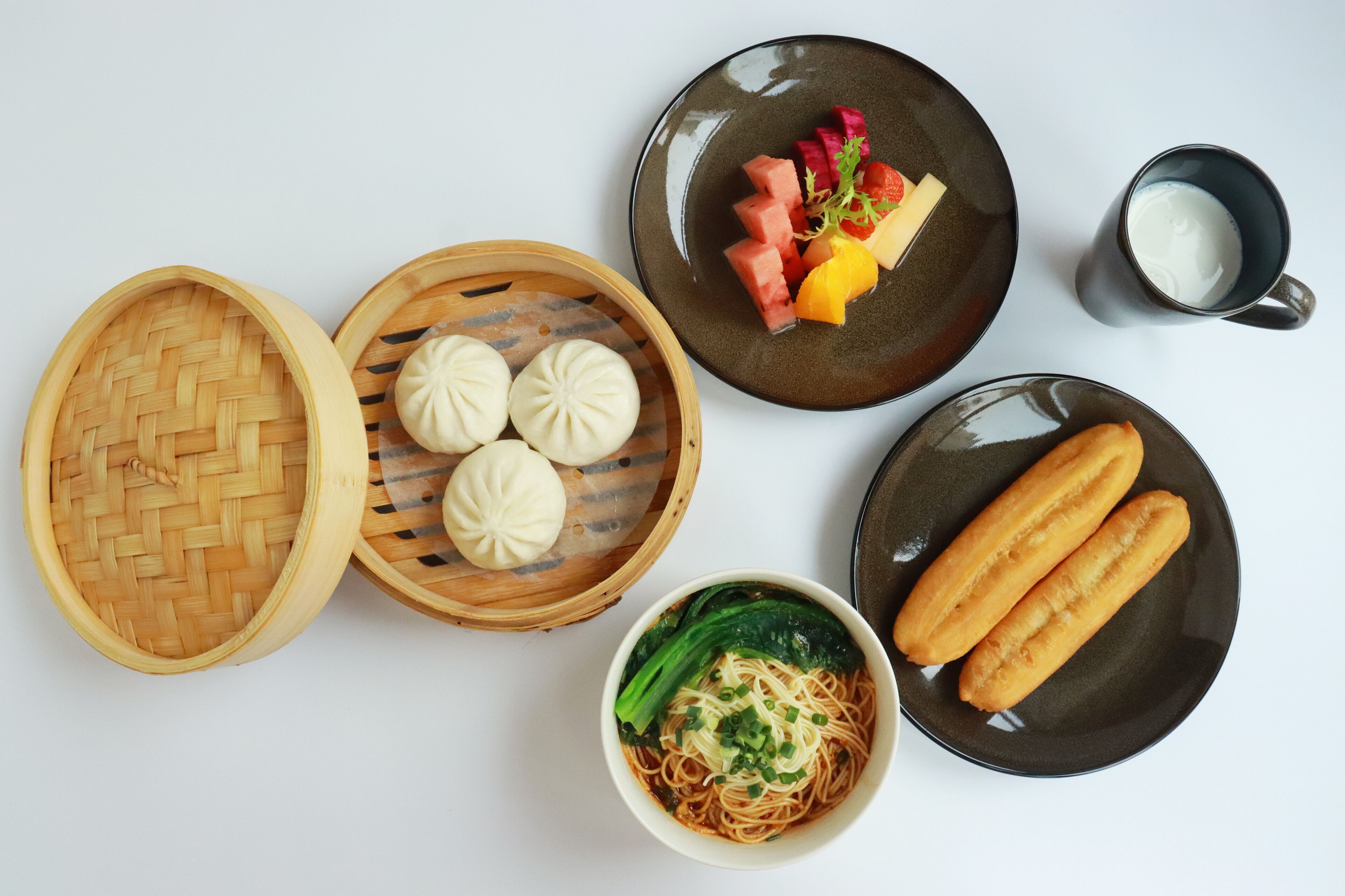 Een tafel met diverse etenswaren, waaronder een kom noedels, dumplings en een bord met fruit en een glas melk.