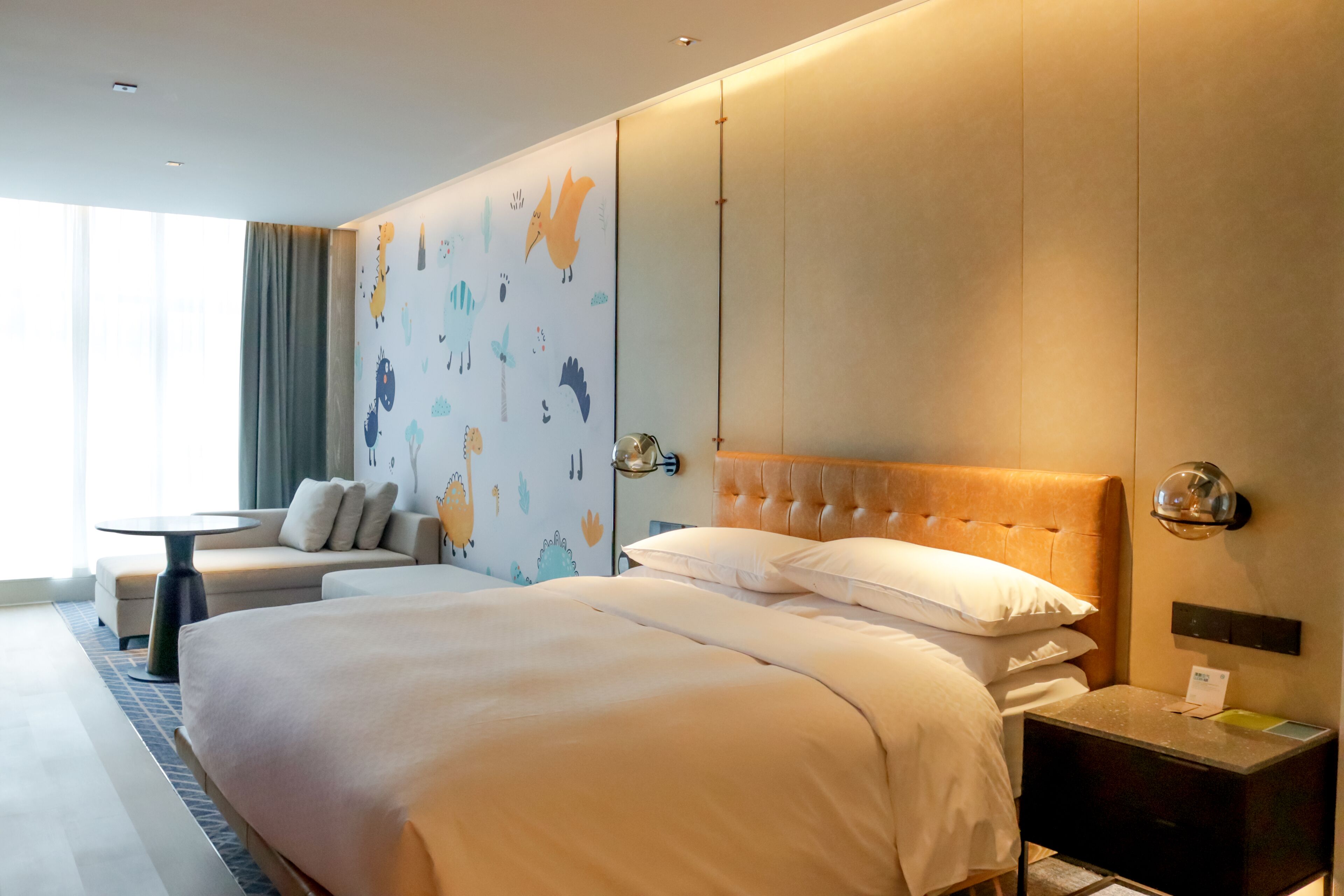 Une chambre d’hôtel avec un grand lit, un canapé, une petite table et un mur décoré d’illustrations d’animaux.