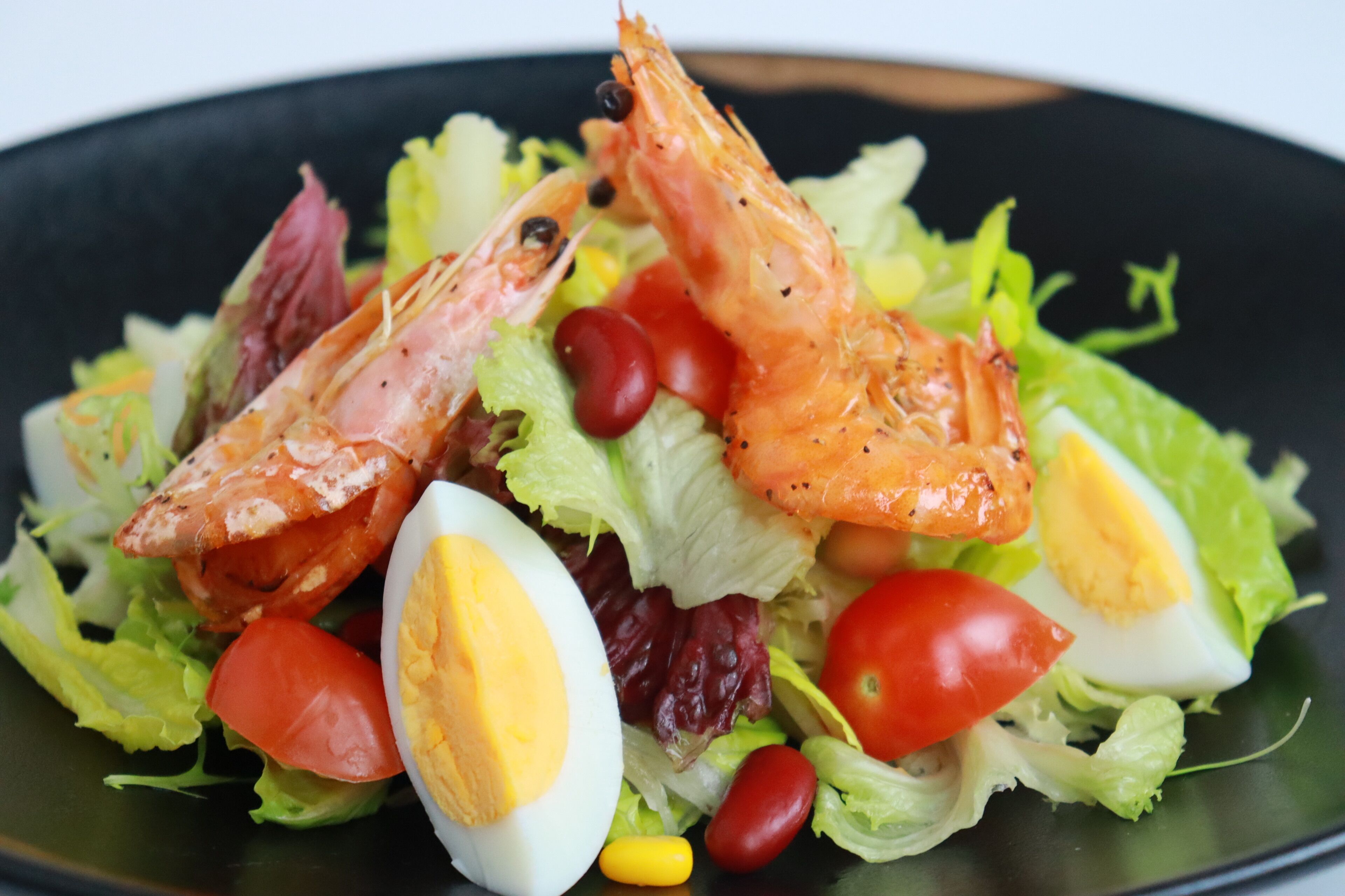 A salad with shrimp, eggs, and vegetables on a plate.
