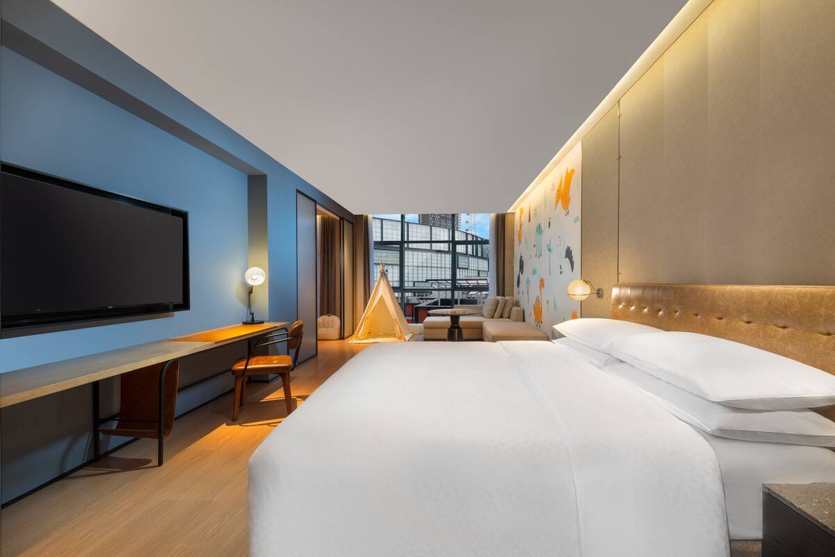 Ein modernes Hotelzimmer mit einem großen Bett, einem Schreibtisch, einem Flachbildfernseher und Blick auf die Stadt.