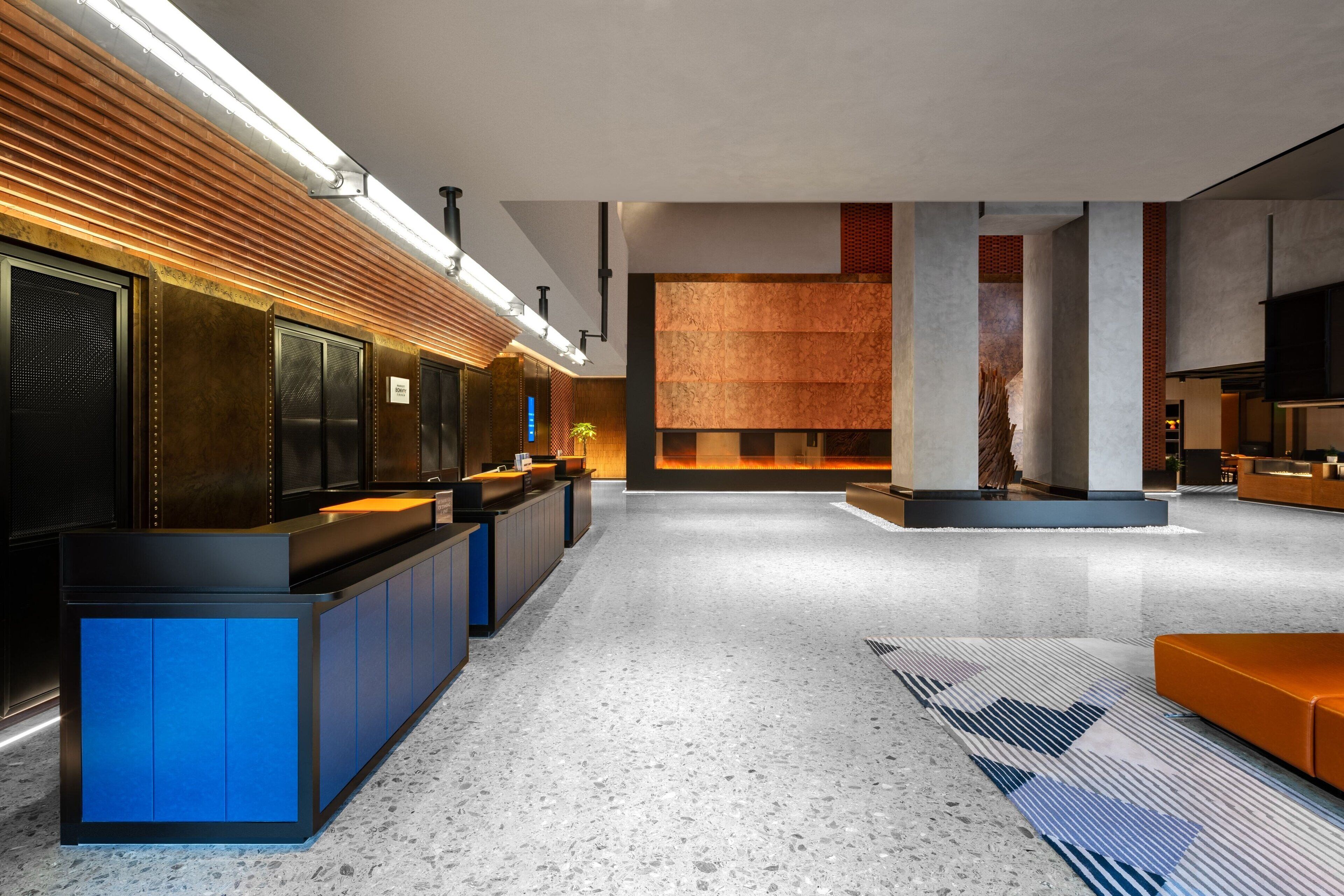 A modern lobby with a reception desk, seating area, and a large wooden panel wall.