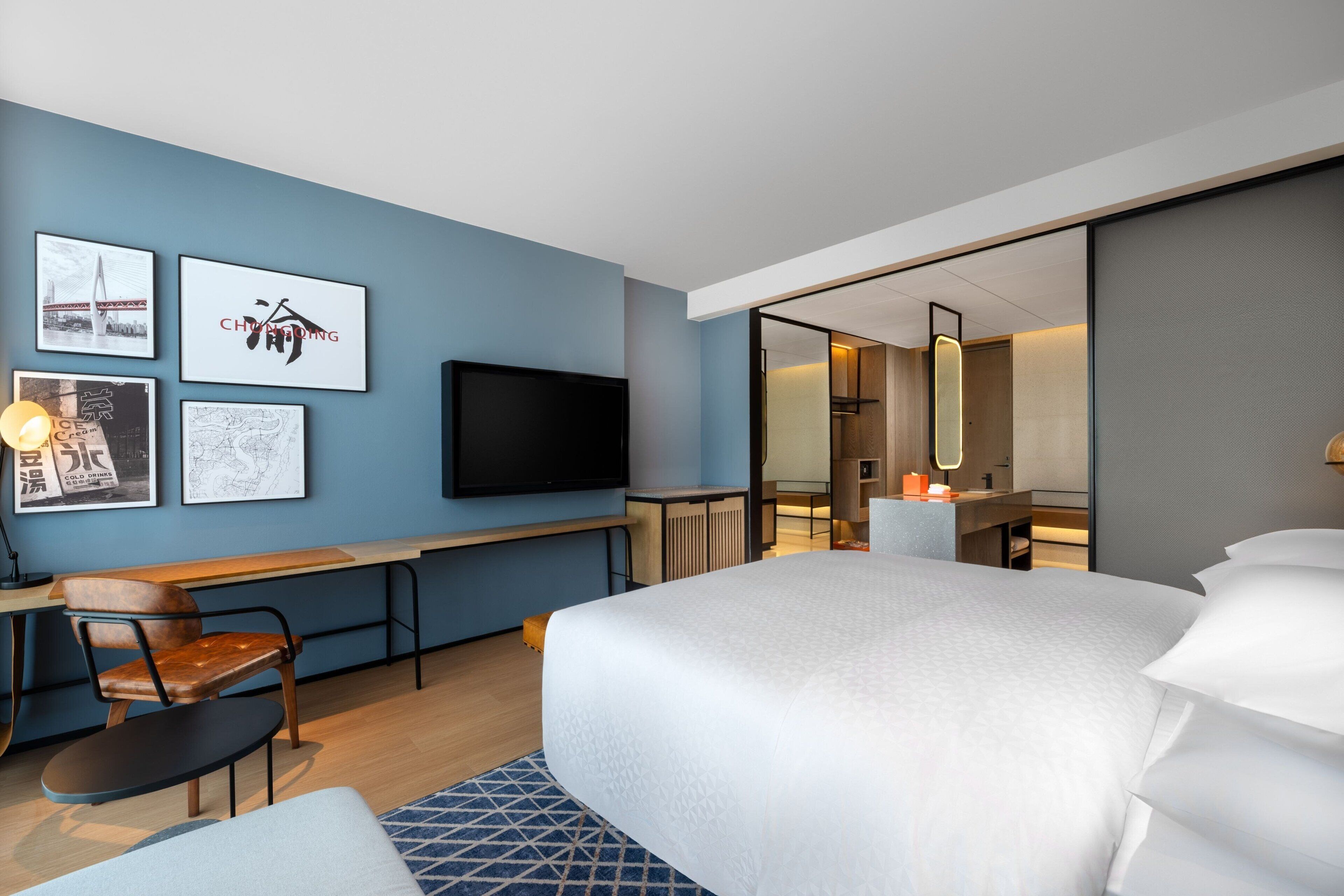 Quarto de hotel moderno com uma cama grande, uma escrivaninha com cadeira, televisão de tela plana e obras de arte nas paredes.