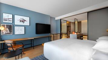 Quarto de hotel moderno com uma cama grande, uma escrivaninha com cadeira, televisão de tela plana e obras de arte nas paredes.