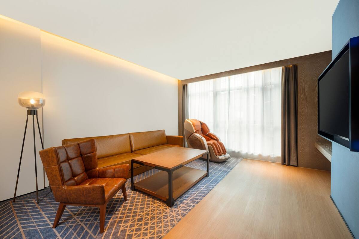 Ein modernes Hotelzimmer mit Sofa, Ohrensessel und Flachbildfernseher.
