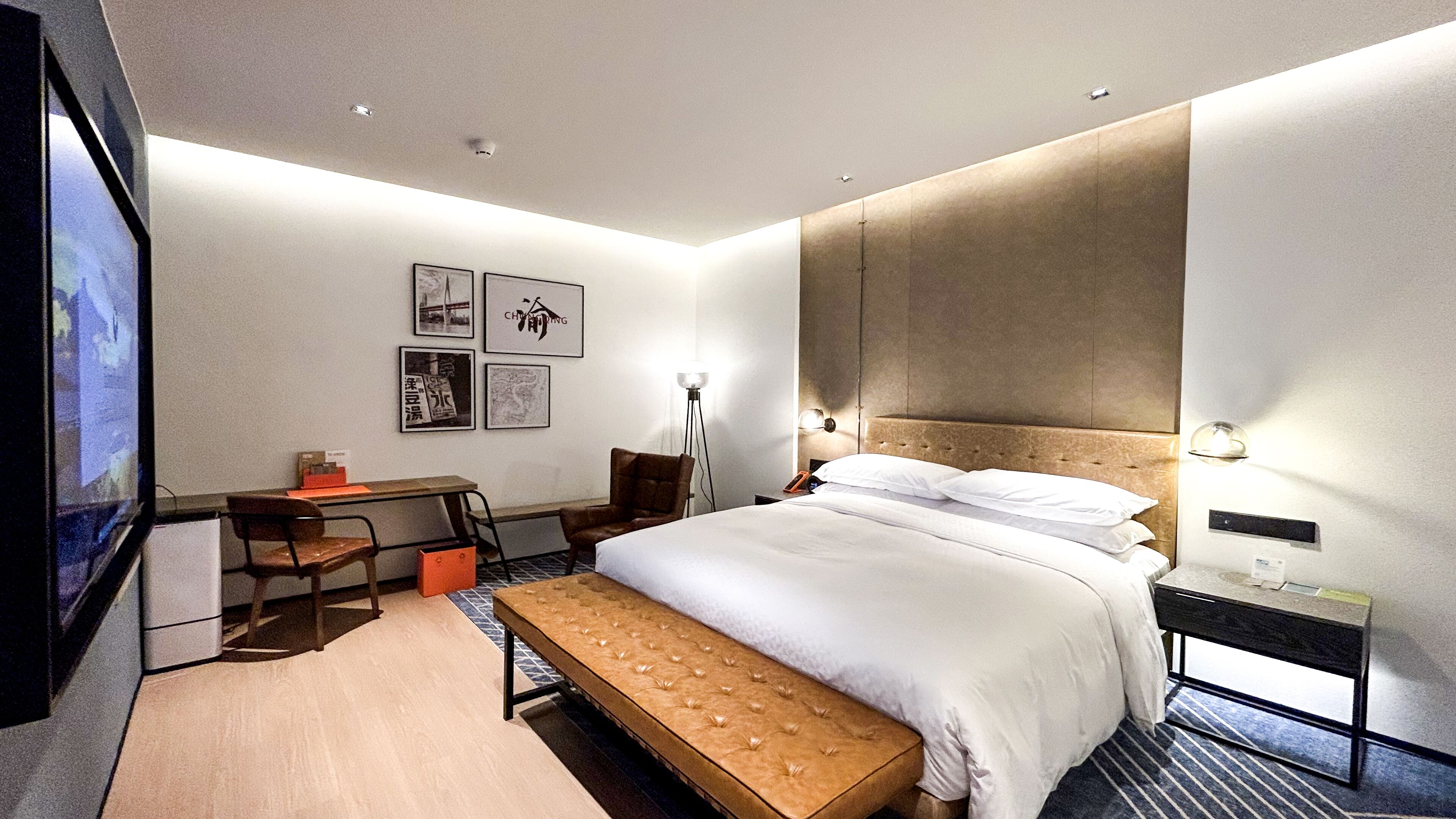 A modern hotel room with a bed, bedside table, desk, chair, and a TV.