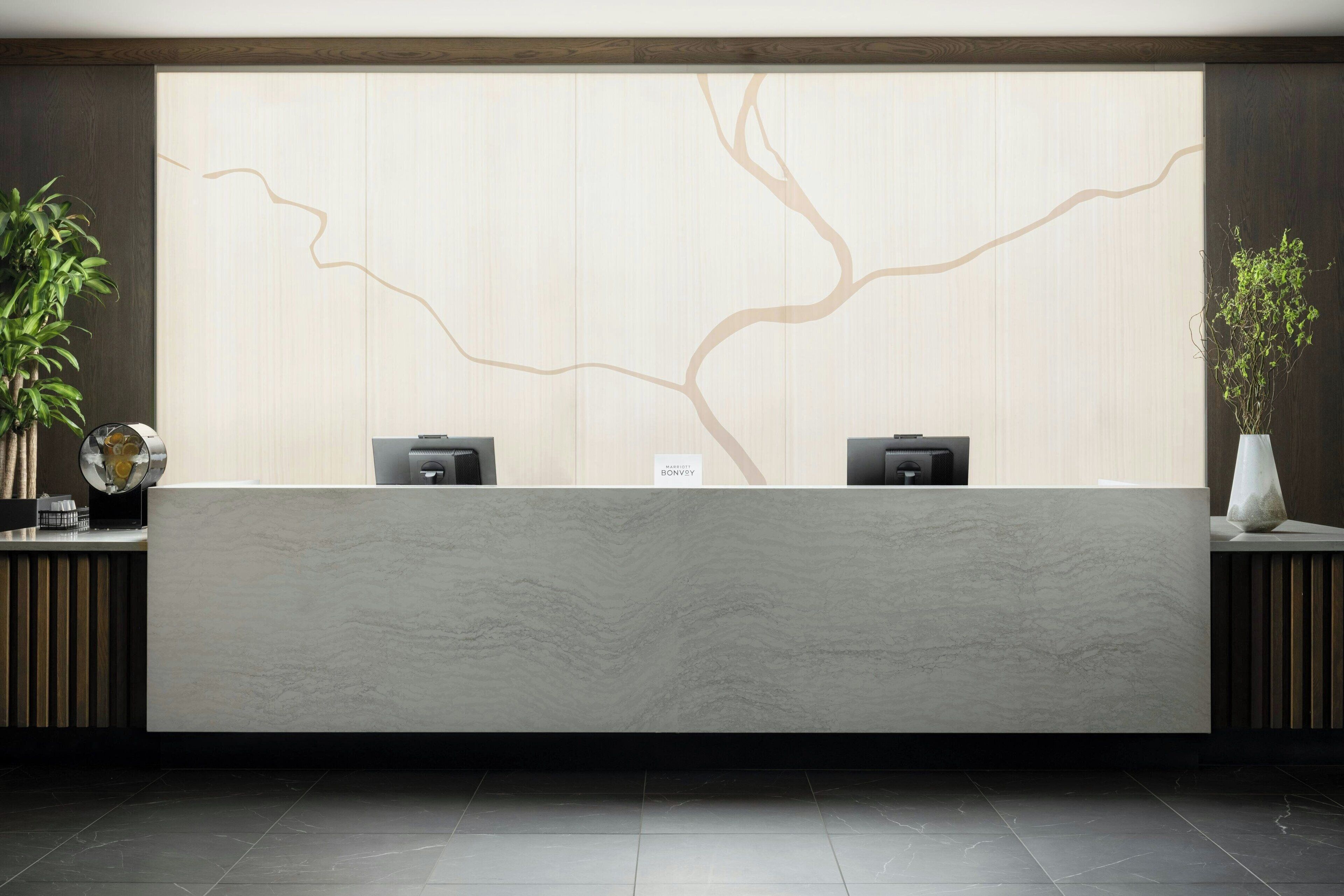 A reception desk with a minimalist design, two black speakers, and a wall with a tree-like pattern.