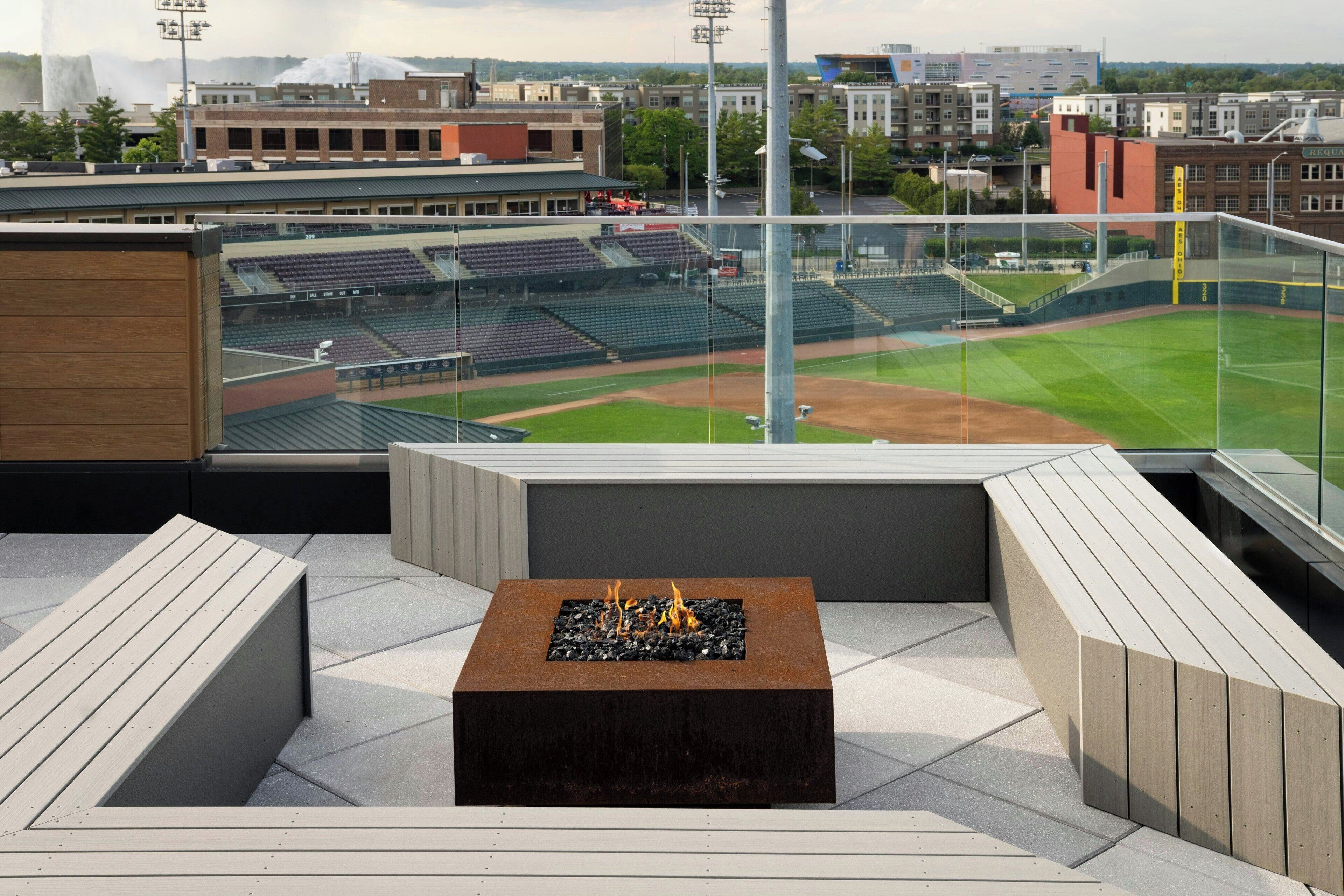 Une terrasse sur le toit dotée d’un foyer, de coins salon et offrant une vue sur un terrain de baseball.