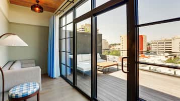 Una sala de estar moderna con un sofá, una butaca y una mesa de madera. Amplios ventanales ofrecen vistas panorámicas de la ciudad.