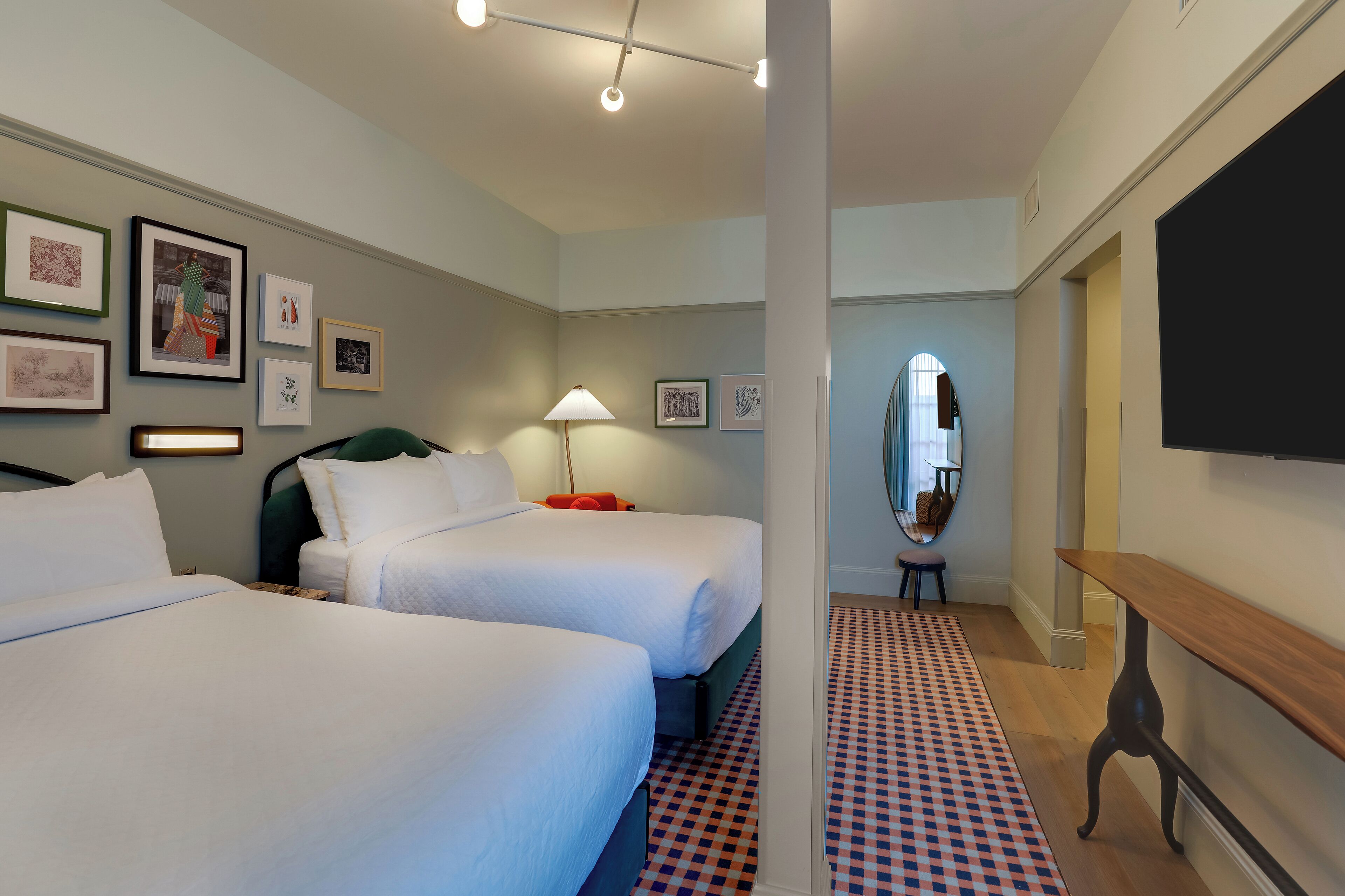 A hotel room with two beds, a desk, a mirror, and wall art.