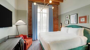 A hotel room with a bed, a desk, a chair, a lamp, and a window with curtains.