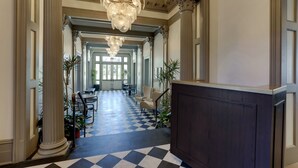Eine Hotelhalle mit Schachbrettmuster-Boden, großen Säulen und einem Kronleuchter.