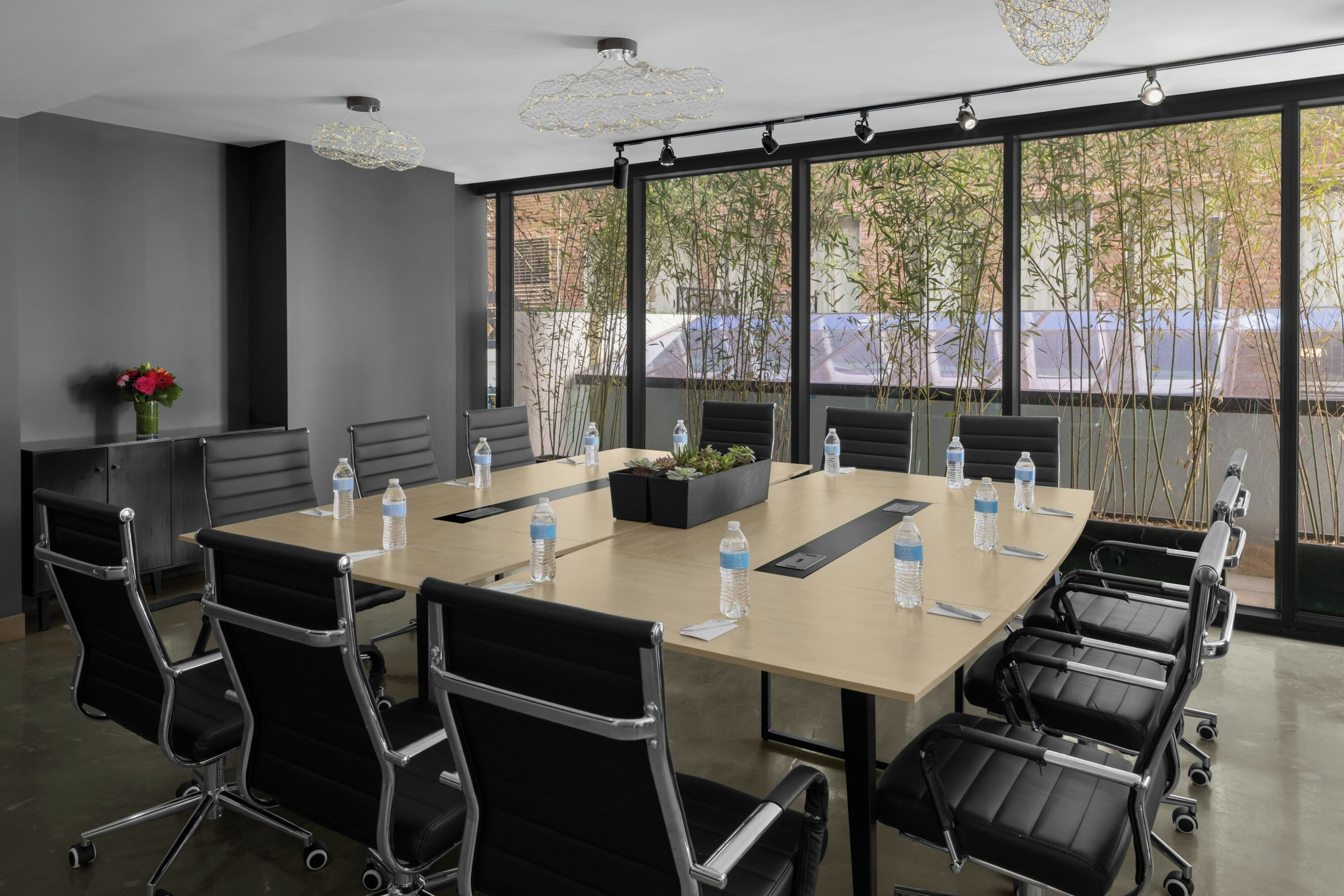 A conference room with a large table, black chairs, and a view of trees through large windows.