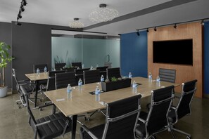 A modern conference room with a long table, black chairs, water bottles, and a large screen on the wall. - Aloft by Marriott New York Chelsea (New York)