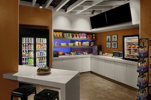 A modern kitchenette with a refrigerator, microwave, and a shelf with snacks. - Aloft by Marriott New York Chelsea (New York)