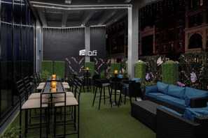 An outdoor seating area with tables and chairs, a blue sofa, and decorative plants. - Aloft by Marriott New York Chelsea (New York)