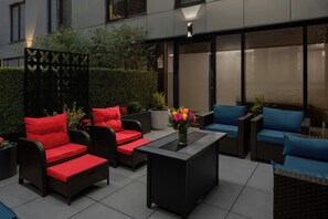 An outdoor seating area with wicker furniture, red cushions, and a vase of flowers.