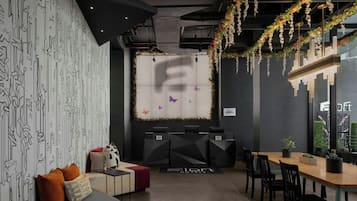 A modern hotel lobby with geometric patterned walls, a reception desk, seating area, and a view of the cityscape through large windows.