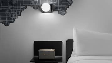 A neatly made bed with a white pillow and a black nightstand with a Marshall speaker.