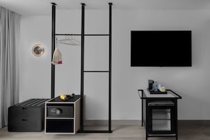 Una habitación moderna con un mueble de almacenamiento negro, un televisor montado en la pared y una pequeña mesa con cafetera.