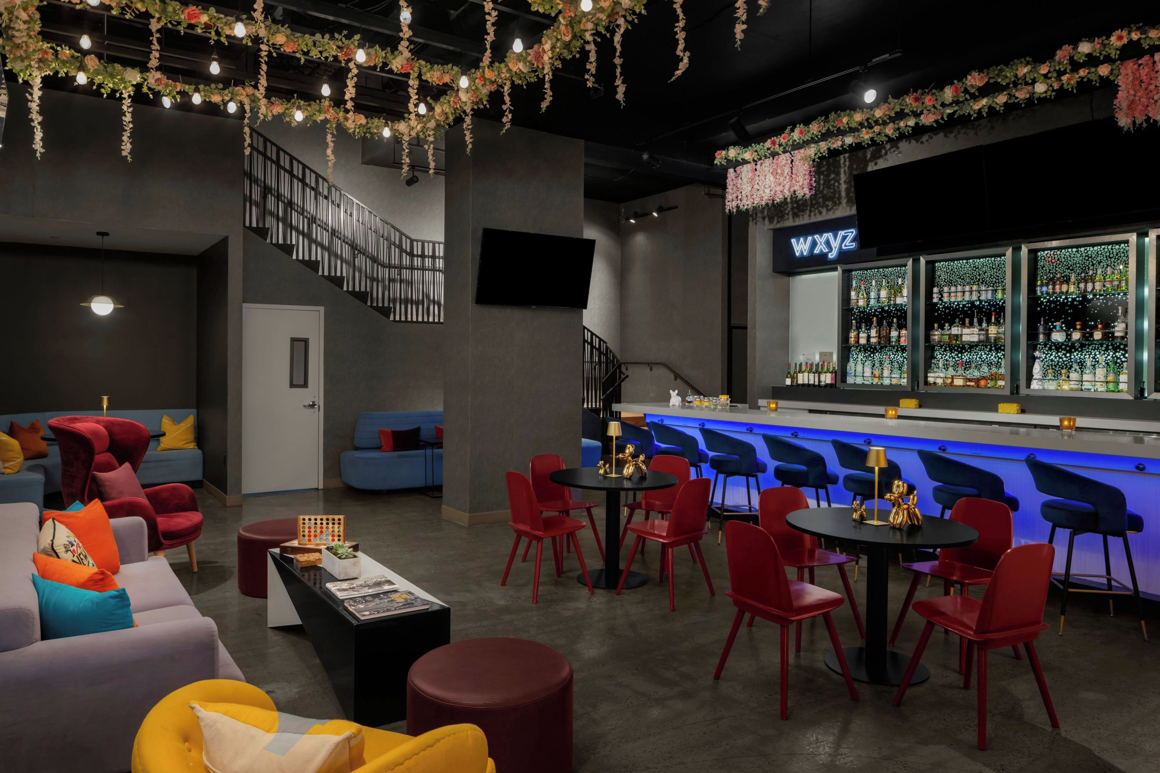 Una zona de bar con barra, sillas rojas y un área de estar con sofás y mesas.