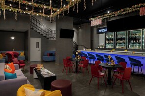 A bar area with a counter, red chairs, and a seating area with sofas and tables. - Aloft by Marriott New York Chelsea (New York)
