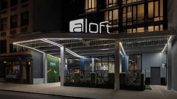 A hotel entrance with a modern design, featuring a prominent awning and string lights.