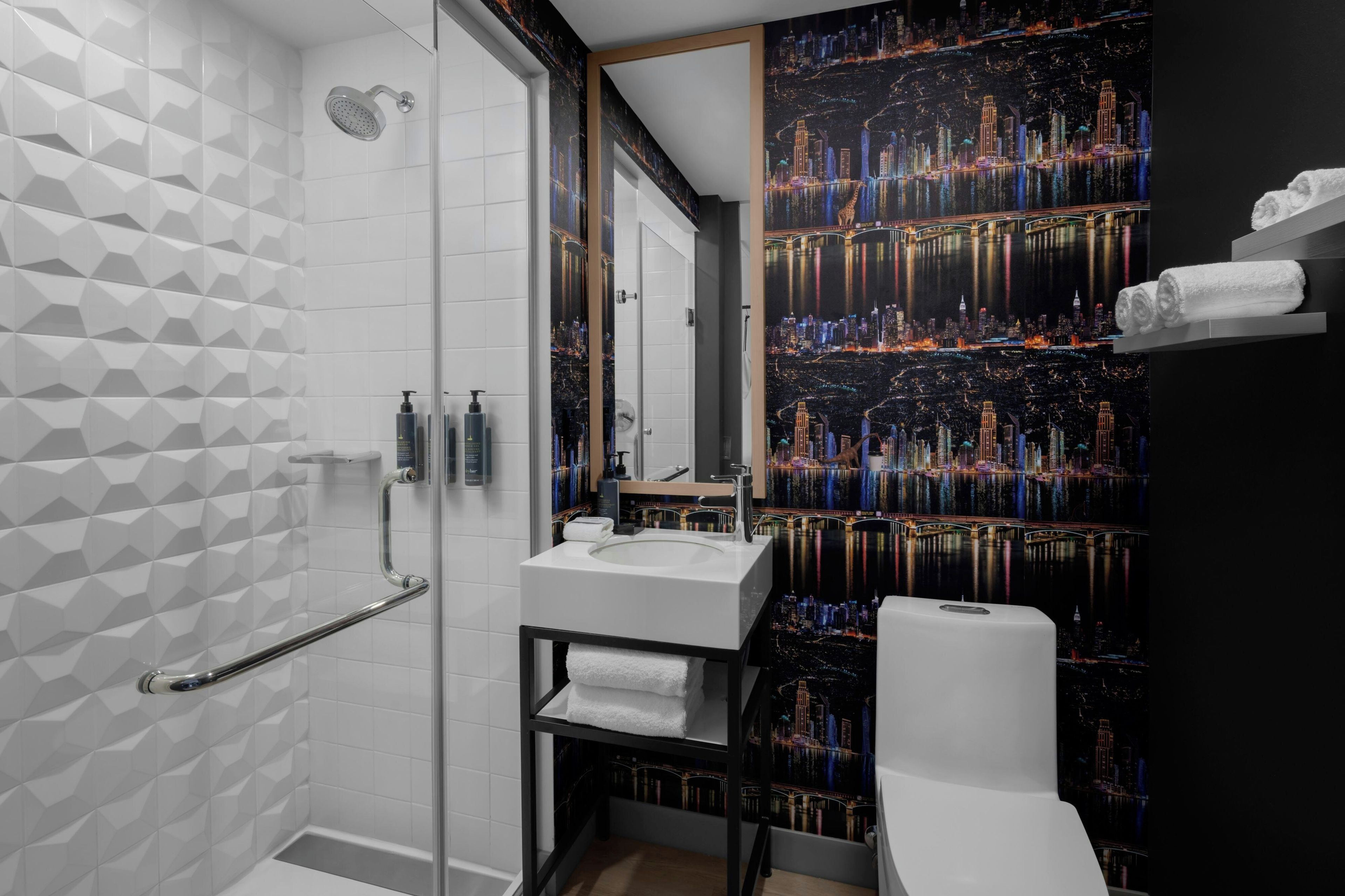 A modern bathroom with a geometric tile pattern, a glass shower enclosure, a white sink, and a large mirror.